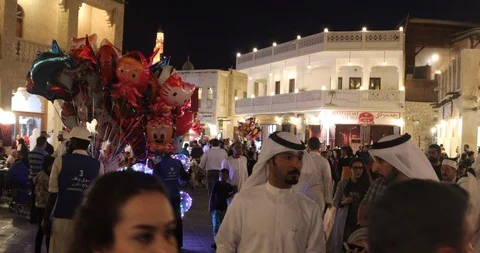 Crowd of people walking in streets of Doha Souq Waqif Qatar flag in background 스톡 동영상 103948699