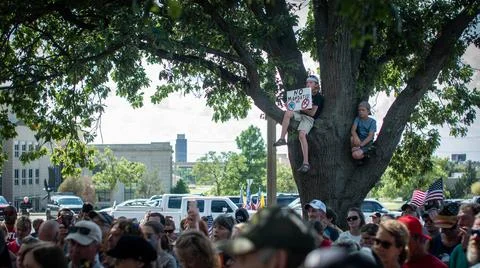 Crowd protesting vaccine mandates with child in tree holding sign Stock Photos