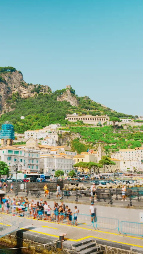 Crowd queueing on a sunlit pier in front of a hillside town of Amalfi Stock Footage 344736159