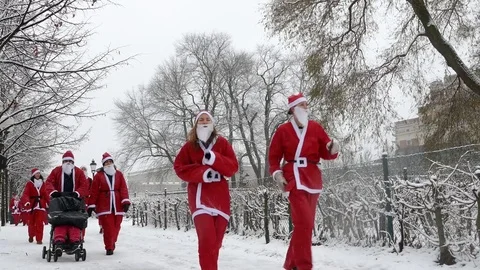 Crowd of Santa Clauses walking running in heavy snow with trees in background Stock Footage 70646463