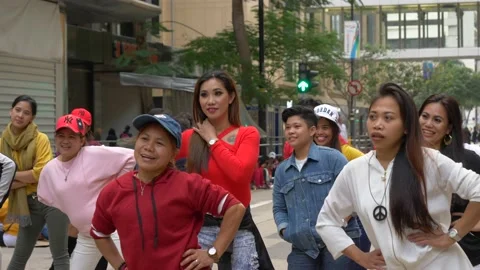 A crowd of smiling people practicing a dance move together on a busy street Stock Footage 146591129
