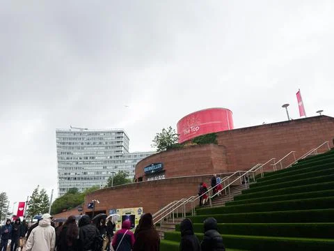 Crowd walking up wet green steps by modern waterfront cultural center with .. Stock Photos