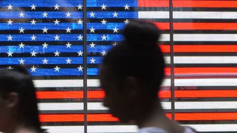 A crowd walks in front a lighting and neon American flag, Time square New York 库存影片 128463882