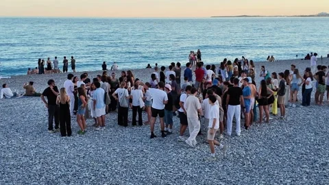 Crowd of young people relaxing on a pebble beach at sunset Stock Footage 336922895