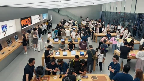 Crowded Apple Store filled with customers exploring new products on sleek wooden Stock Footage 339329515