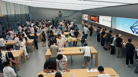 Crowded Apple Store filled with customers exploring new products on sleek wooden Stock Footage 339329516