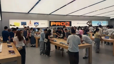 Crowded Apple Store filled with customers exploring new products on sleek wooden Stock Footage 339329524