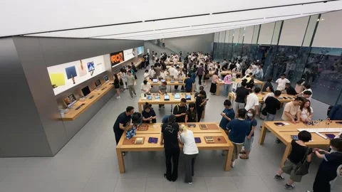 Crowded Apple Store filled with customers exploring new products on sleek wooden Stock Footage 339329545