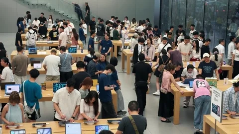 Crowded Apple Store filled with customers exploring new products on sleek wooden Stock Footage 339329561