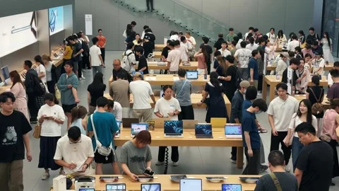Crowded Apple Store filled with customers exploring new products on sleek wooden Stock Footage 339329564