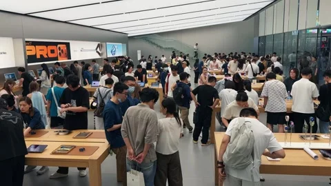 Crowded Apple Store filled with customers exploring new products on sleek wooden Stock Footage 339329581