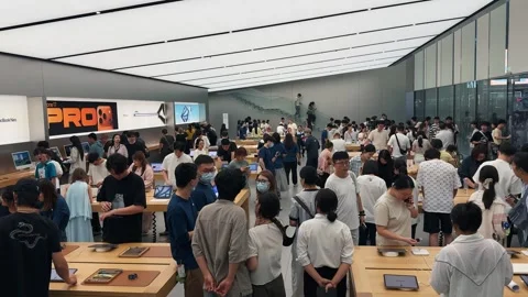 Crowded Apple Store filled with customers exploring new products on sleek wooden Stock Footage 339329583