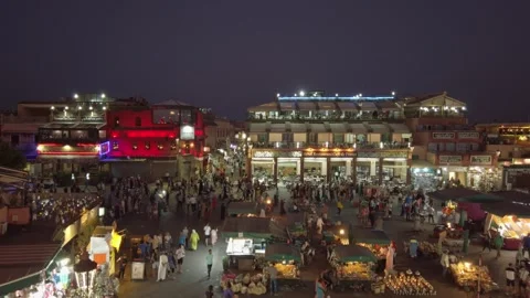 Crowds gather around colorful evening market stalls in Marrakech's Jemaa el-Fnaa Stock Footage 336757151