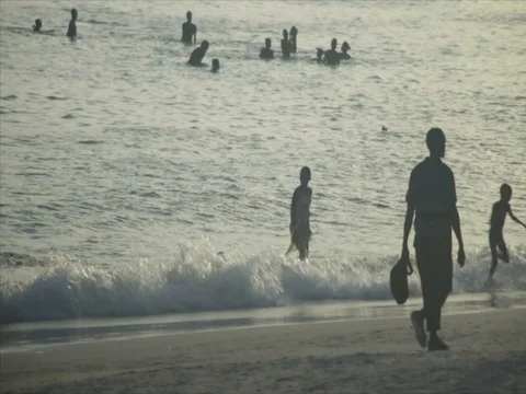 Crowds of locals walk down the beach as children play in the ocean in Kenya. Stock Footage 85012697