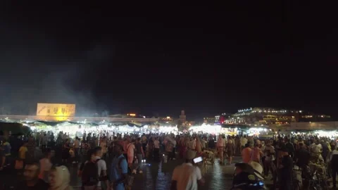 Crowds move through illuminated stalls in Marrakesh's Jemaa el-Fnaa at dusk Stock Footage 336506081