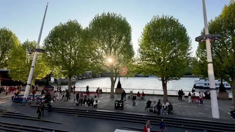 Crowds relax and stroll along London’s Southbank riverfront at golden hour 動画素材 334294195