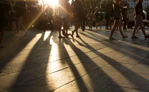 Crowds walking in a district as sun flares between them in the late afternoon Stock Photos