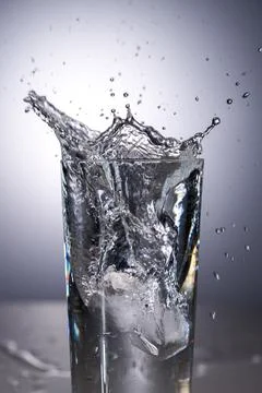 A crown-like splash created when an ice cube enters the water. Stock Photos