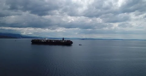 Cruising around container ship approaching harbour on a cloudy day Stockbeeldmateriaal 75476582