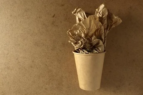 Crumbled paper inside a brown cup placed on a plain surface in a simple indoor Stock Photos