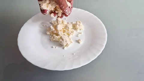 Crumbling Fresh Cottage Cheese by Hand onto White Plate Stock Footage 337286311