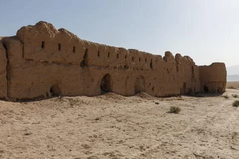The crumbling mud brick wall of an ancient caravanserai stands in arid desert Stock Photos
