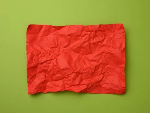Crumpled rectangular sheet of red paper on a green background, top view 스톡 사진
