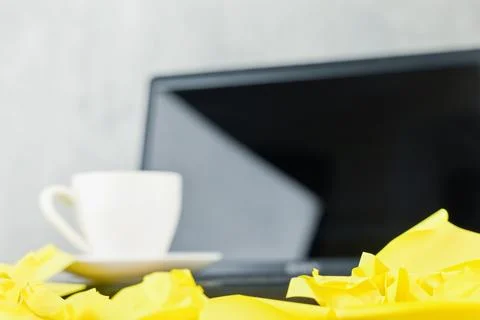 Crumpled yellow notes sit in front of a coffee cup and blurred laptop Stock Photos