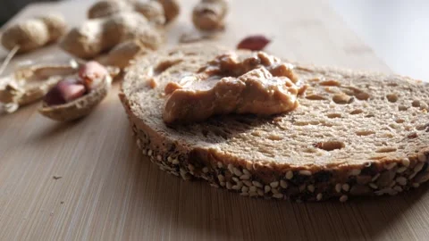 Crunchy peanut butter spread on a slice of seeded bread with peanuts in the Stock Footage 298187824