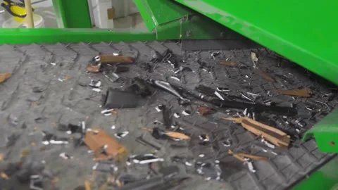 Crushed and destroyed firearms exiting a grinder on a conveyor belt Video stock 333680865