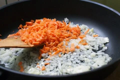 Crushed onions and carrots in a frying pan and wooden spatula. homemade dishe Stock Photos