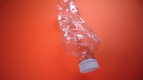 Crushed plastic bottle with cap lies on bright orange Stock Footage 136778904