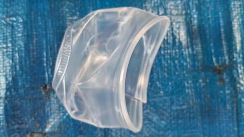 Crushed translucent plastic cup lying on a textured blue surface Stock Photos