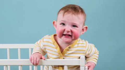 Cry infant baby boy stands in the crib, studio blue background. Sad child in yel Stock Footage