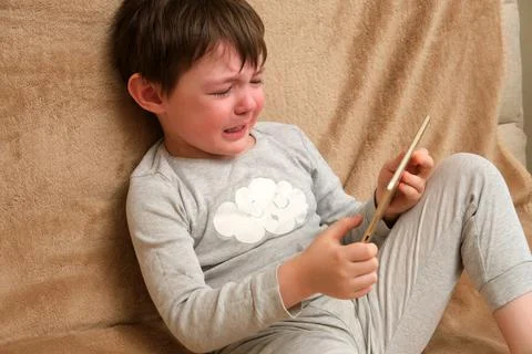 Crying boy holding a digital tablet. Child problem with screen time and techn Stock Photos