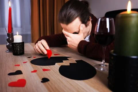 Crying man with face in hand sitting at table with wine and broken black he.. Stock Photos