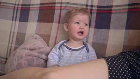 Crying toddler sitting on a couch with plaid background and soft pillow, capturi Video stock 320635408