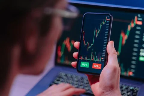 Crypto trader analyzing live cryptocurrency and stock charts on smartphone Foto stock