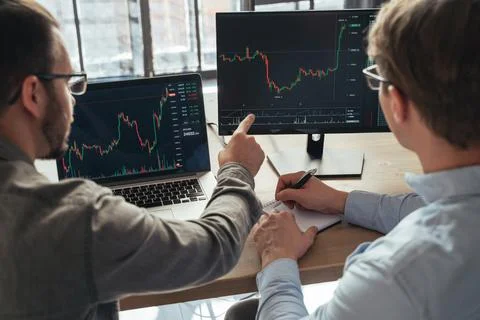 Crypto traders sitting together in front of PCs, monitoring candlestick charts Stock Photos