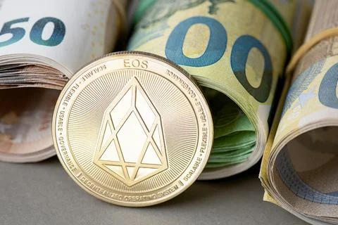 Cryptocurrency EOS golden coin on the background of rolled euro bills. Foto stock