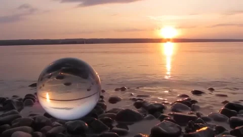 Crystal Ball Reflection of Golden Sunset Over Water on Pebble Beach Stock Footage 323104536