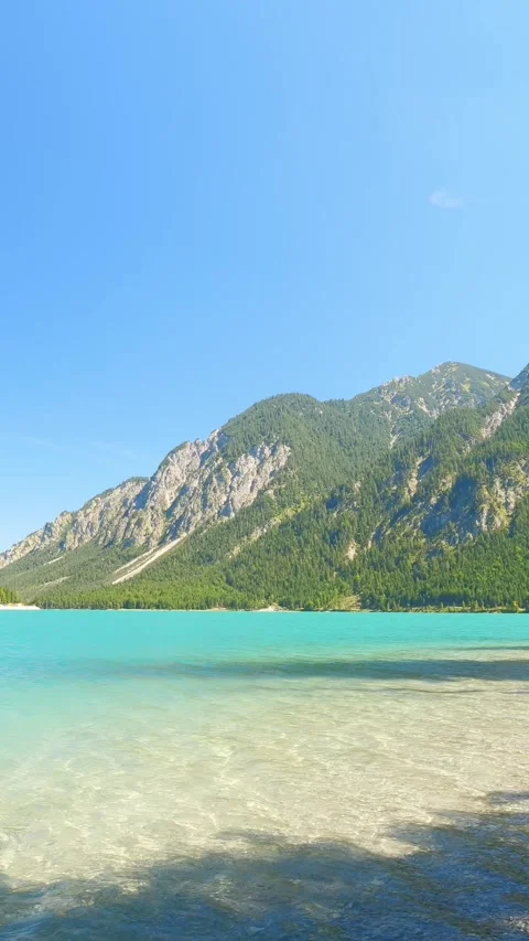 Crystal clear blue lake surrounded by forested alpine ridges and grassy lakes Stock Footage 308301446