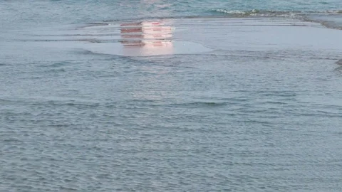 Crystal clear blue Ocean Waves washing onto a sandy beach reflecting Lighthouse Stock Footage 117412898