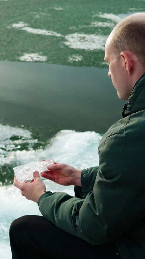 Crystal clear ice in the hands of a man sitting on the shore of a lake. Stock Footage 344021017