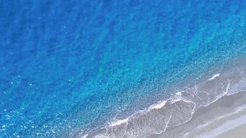 Crystal Clear Ocean Waves Gently Lap Against a Sandy Shoreline During a Sunny Stock Footage 317760678