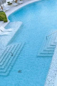 Crystal clear pool with steps and a slide at a luxury resort on a sunny day Stock Photos