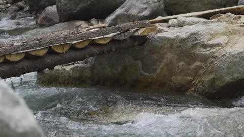 A crystal clear river flows under a wooden bridge, crashing against rocks Video stock 280266211
