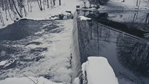 Crystal-Clear River next to a Waterfall with Falling Snowflakes Stock Footage 300022976