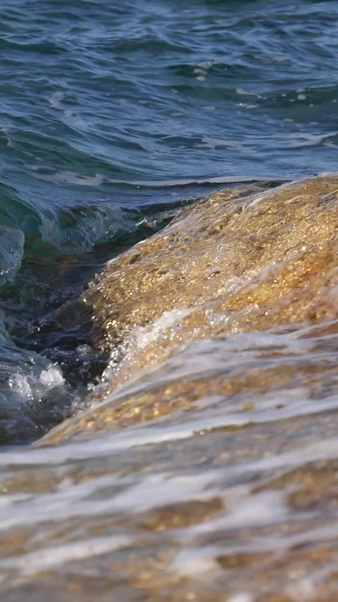 Crystal clear sea waves gently crash onto golden coastal rocks. Stock Footage 337417252