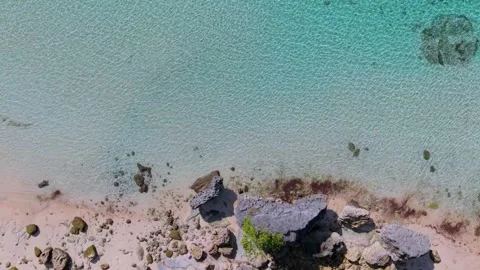 Crystal clear turquoise sea water gently lapping a sandy beach with rocks Video stock 336649341